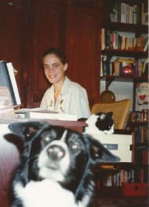 teenage me sitting at my desk with lots of books in the background and my pet dog jack photobombing me